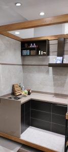 Modern kitchen display with dark wood cabinets, beige countertop, wall-mounted open shelving, and marble-effect wall tiles
