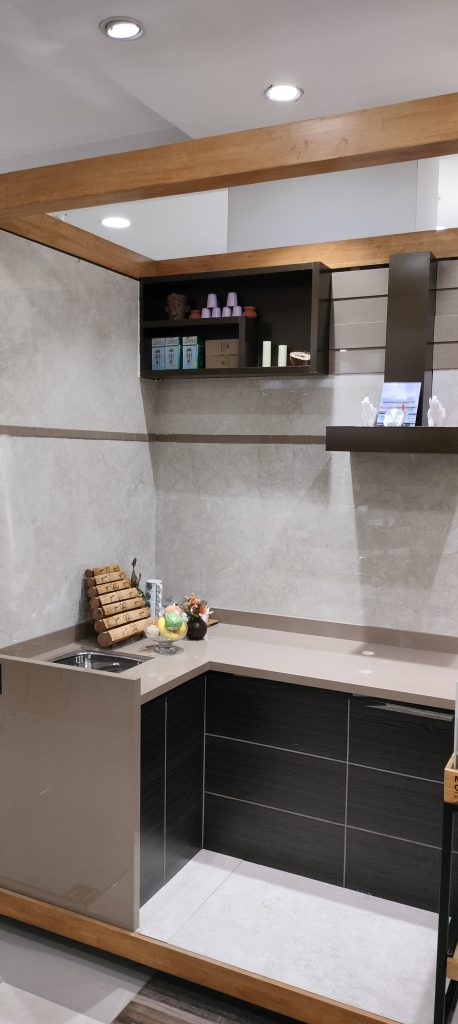 Modern kitchen display with dark wood cabinets, beige countertop, wall-mounted open shelving, and marble-effect wall tiles