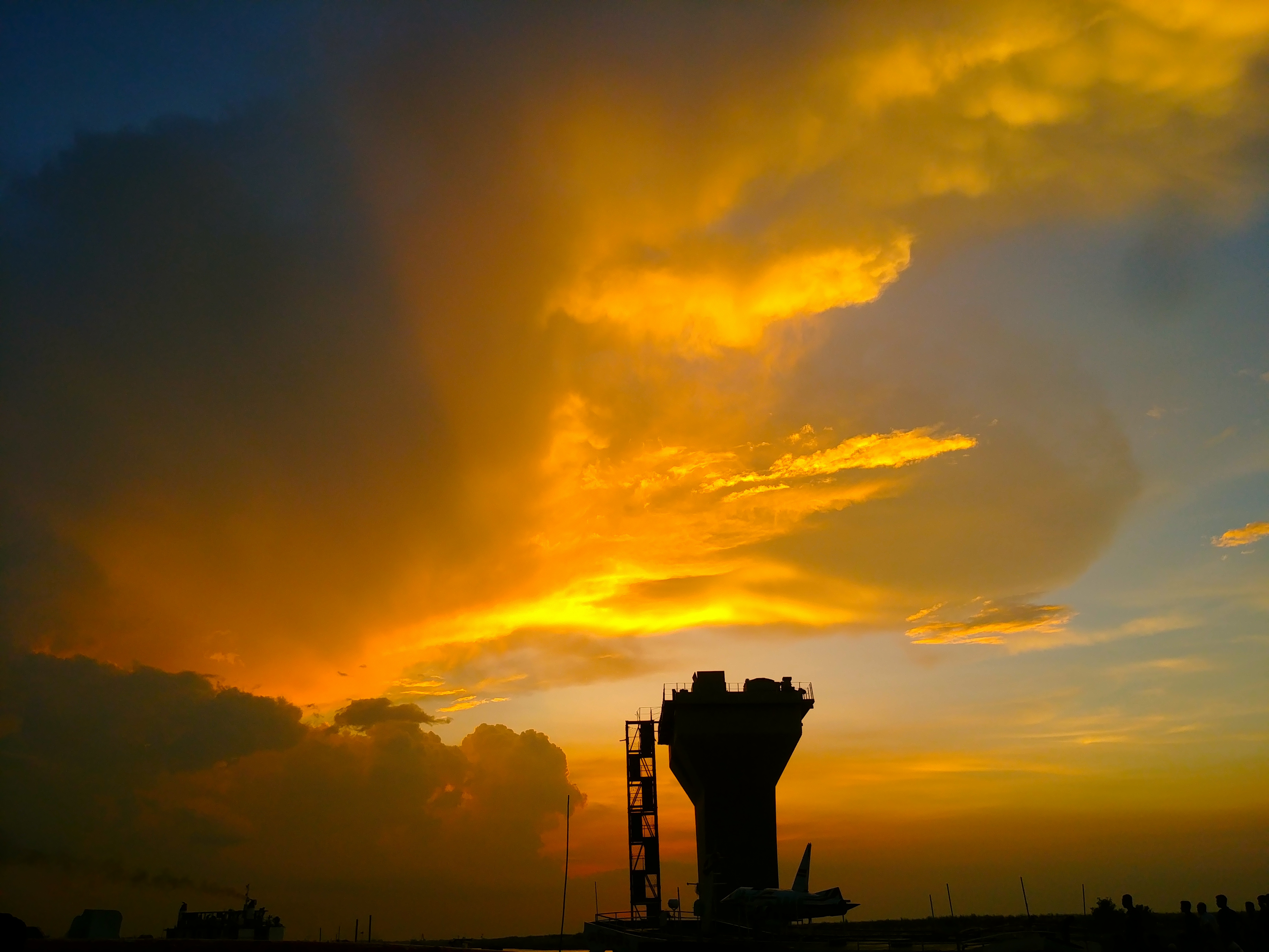 Vibrant sunset with large, glowing orange clouds contrasting a deep blue sky, casting a silhouette of a rooftop and antenna, creating a serene atmosphere.