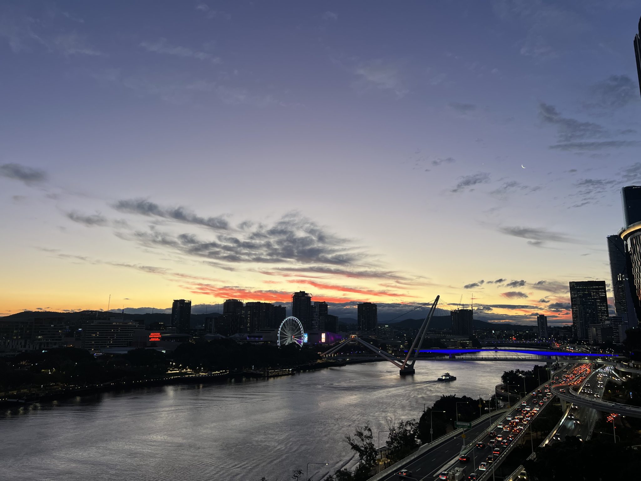 A wide shot of city skyscrapers and a river under a colorful sunset sky.