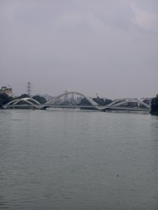 Modern Hatirjheel Bridge spanning calm lake waters in Dhaka, Bangladesh, with a cloudy sky, urban skyline, and peaceful waterfront atmosphere.