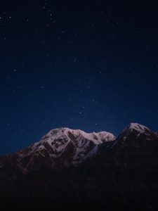 Snow capped mountains under a starry night sky. The serene scene conveys tranquility, with stars bright against the deep blue backdrop.