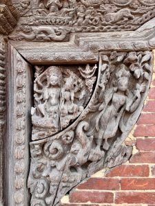 Aged wooden temple corner carving depicting a multi-armed goddess (possibly Lakshmi or Tara) with attendant figures on a cracked tympanum panel, Nepal. 