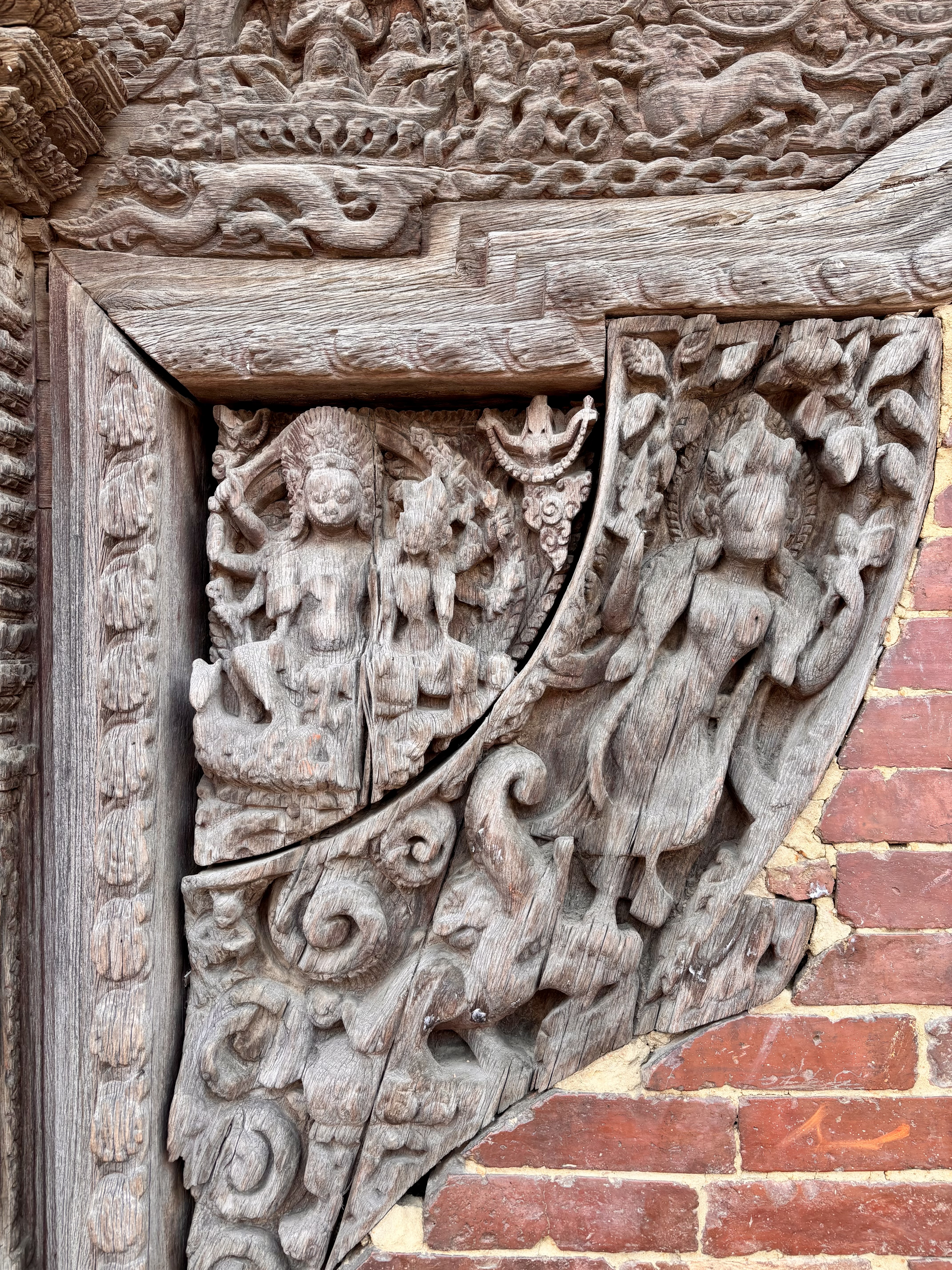 Aged wooden temple corner carving depicting a multi-armed goddess (possibly Lakshmi or Tara) with attendant figures on a cracked tympanum panel, Nepal.