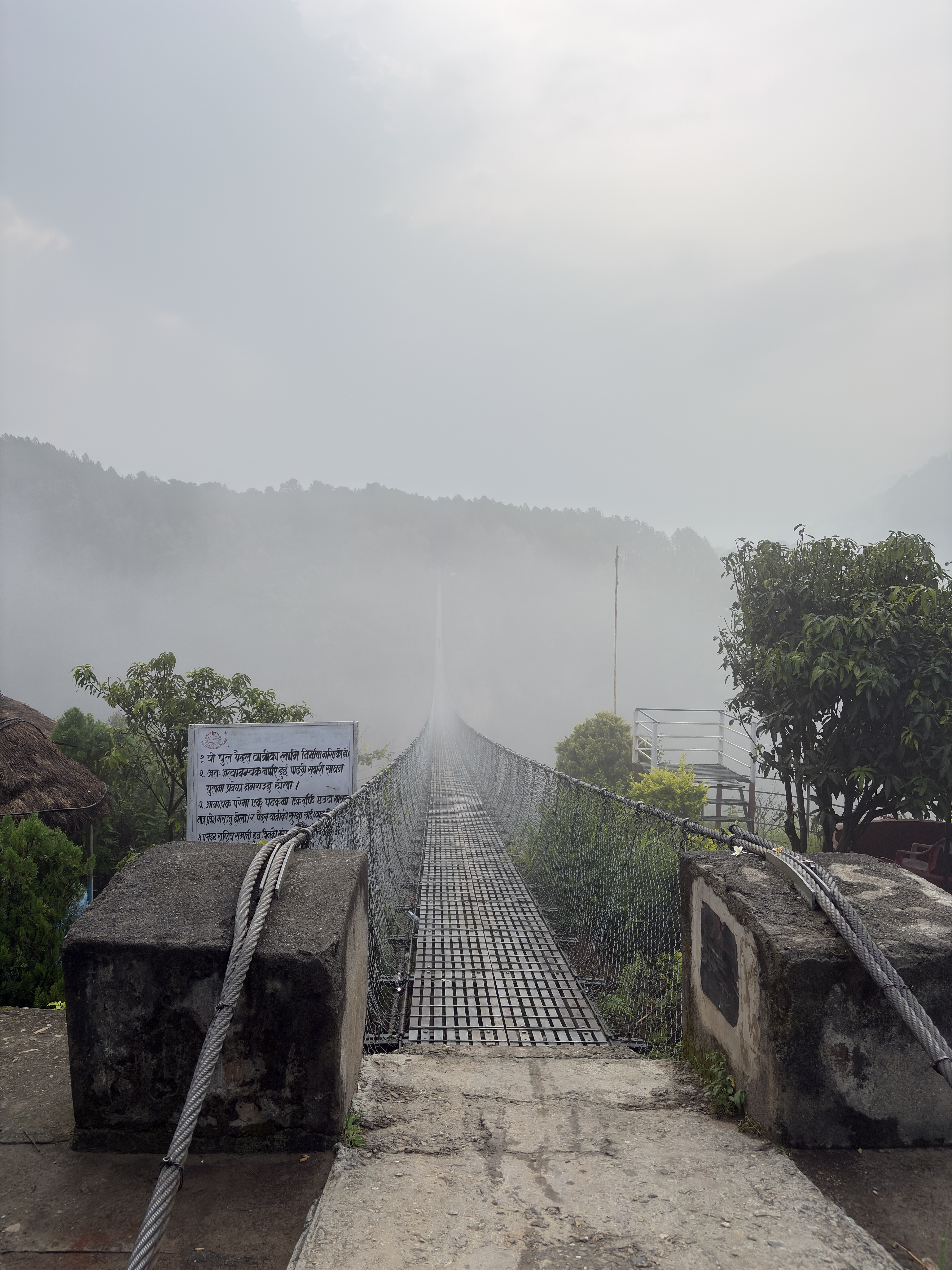 Suspension footbridge vanishing into misty mountain fog in Nepal