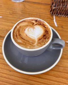 A cappuccino with intricate heart-shaped latte art dusted with cinnamon, served in a grey ceramic cup and saucer. 