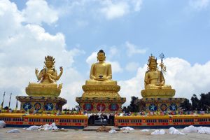Golden statue of Buddha seated in serene meditation, flanked by bodhisattvas, radiating peace and spiritual devotion under the Himalayan sky. 