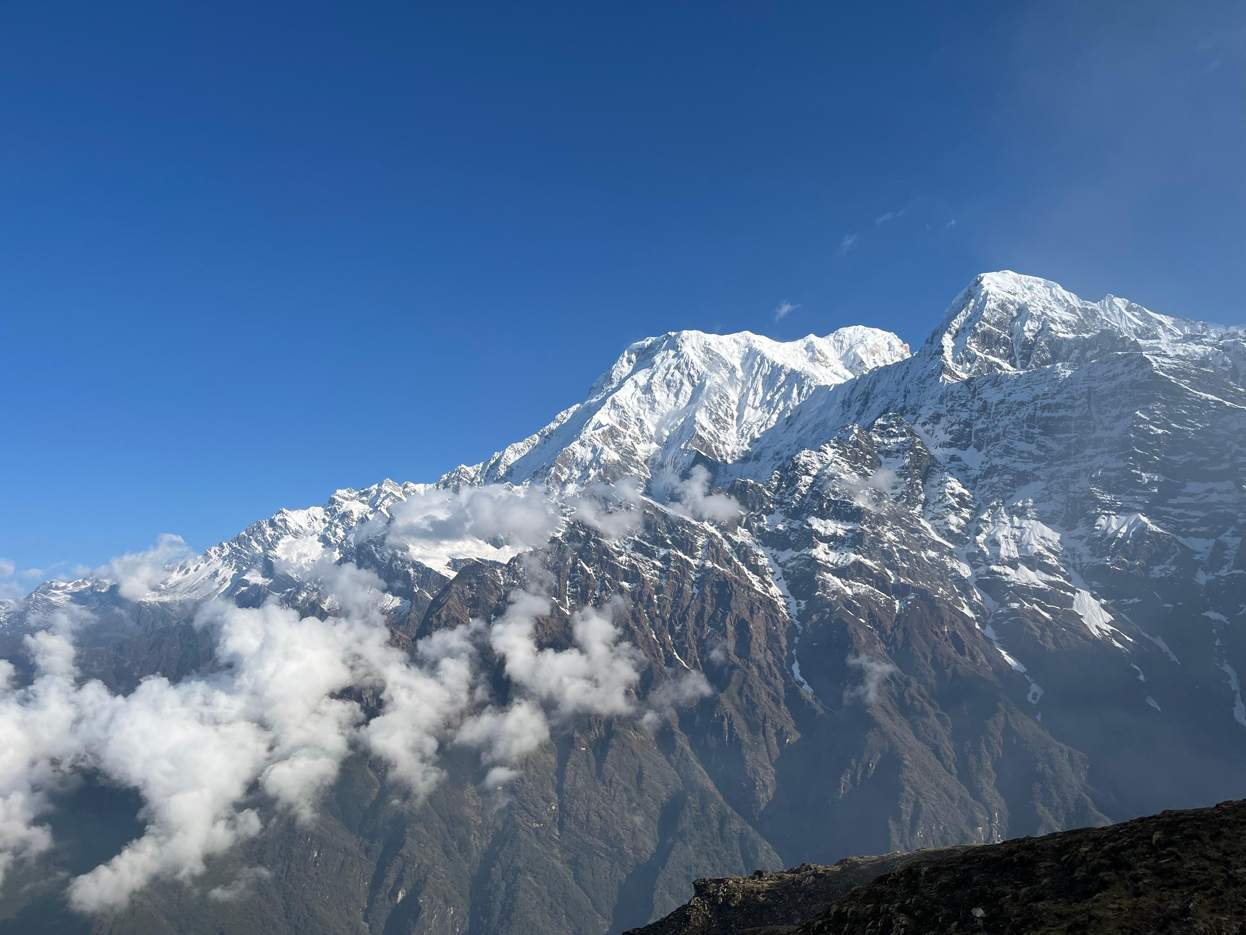 Snow-capped mountains rise under a clear blue sky, with fluffy white clouds partially covering the peaks.