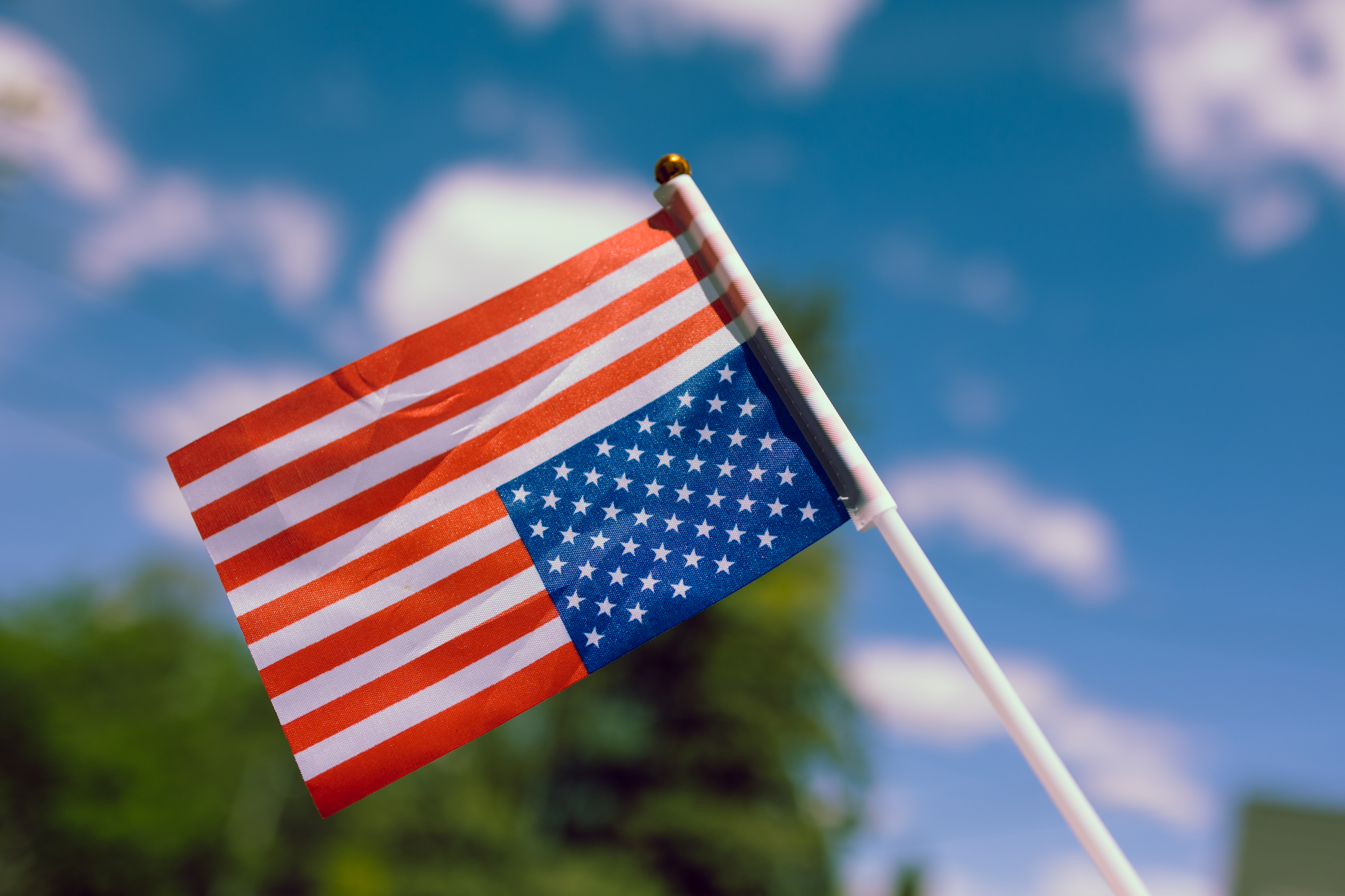 Upside Down United States flag, a symbol of dire distress, with a few clouds and some trees in the background
