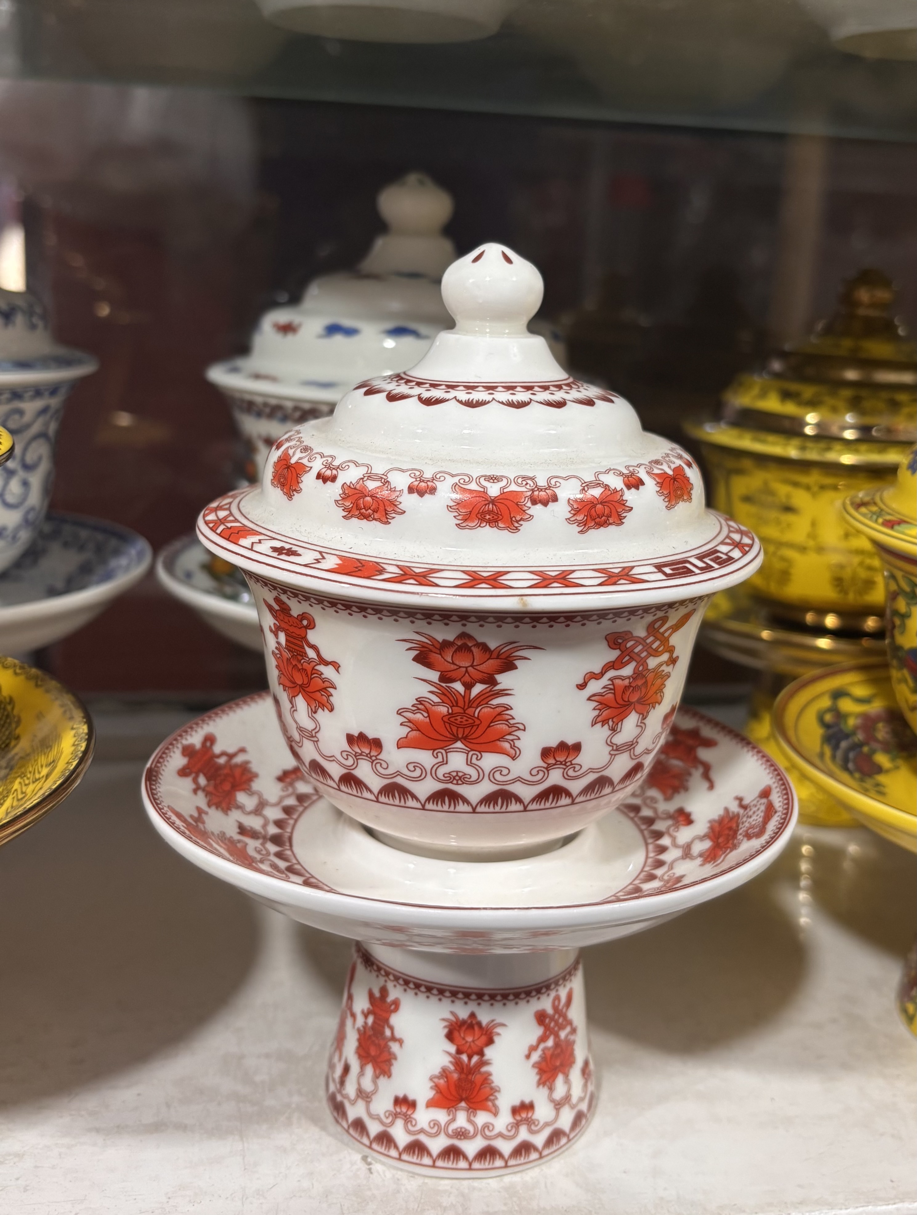 Porcelain teacup with lid on matching saucer, adorned with intricate red floral and geometric patterns.