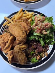 Plate of fried chicken with French fries, salad, and rice.