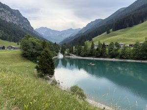 View of Gänglesee in Malbun, Liechtenstein, surrounded by alpine mountains, forested slopes, and clear natural scenery.
