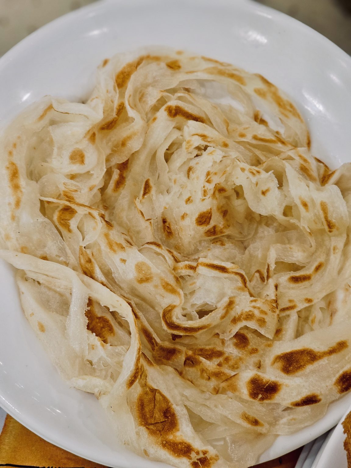 Soft, flaky Kerala porottas with golden, toasted layers, freshly prepared and ready to enjoy with curry. A popular South Indian favorite. Captured in Palazhi, Kozhikode, Kerala.