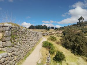 Road at Puca Pucara, an Inca archaeological site near Cusco, with a stone wall, grassy landscape, and open sky.