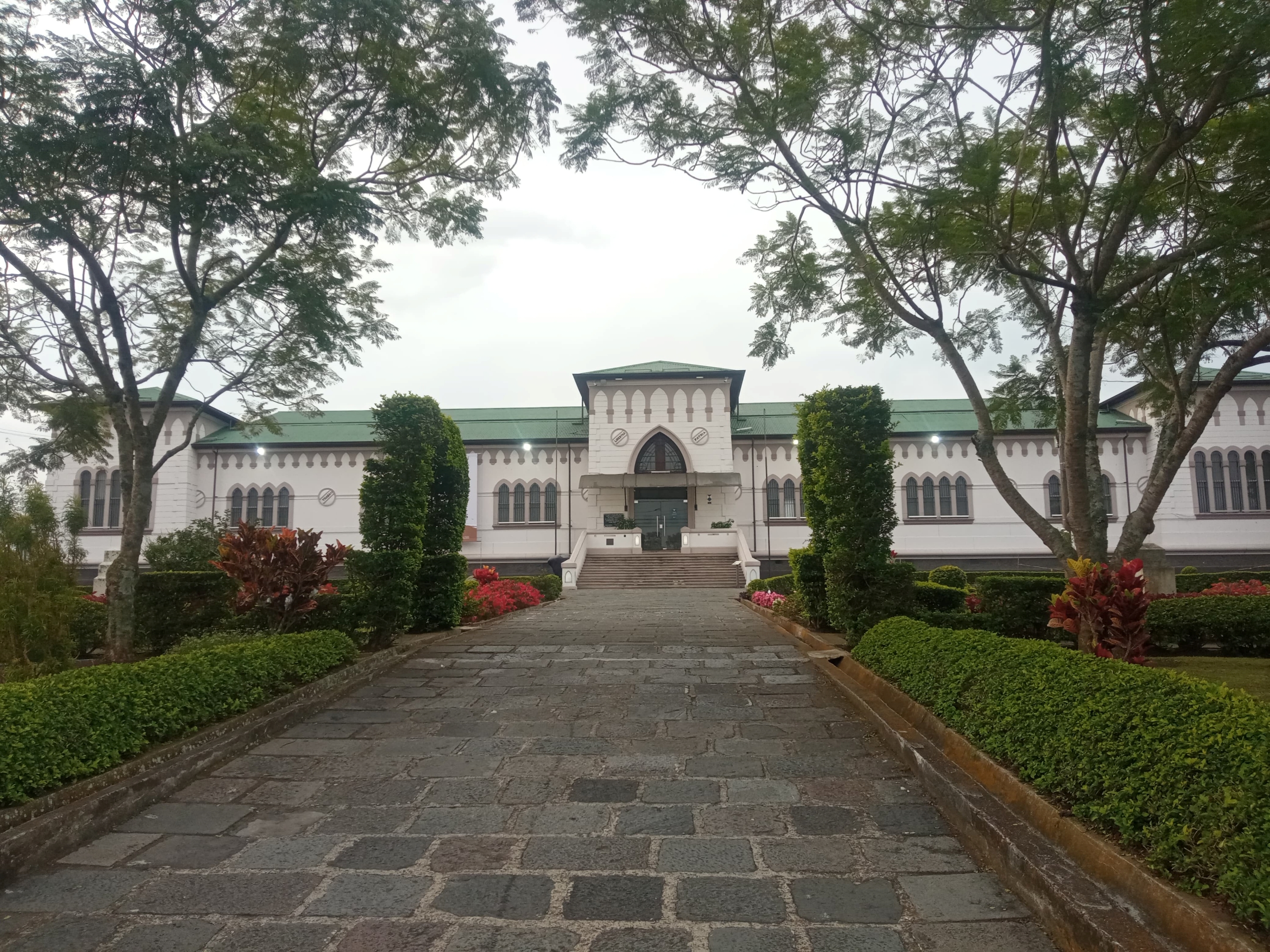 Front entrance of the Municipal Museum of Cartago, Costa Rica. Historic building with Gothic-style architecture, green roof and arched windows, framed by a stone pathway and lush garden landscaping.