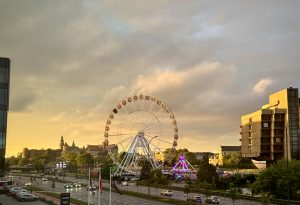 Ferris wheel illuminated at sunset with dramatic storm clouds over the skyline of Kraków, Poland.
