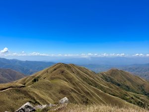 Colinas cubiertas de pasto con rocas en primer plano y un cielo azul con nubes en el horizonte