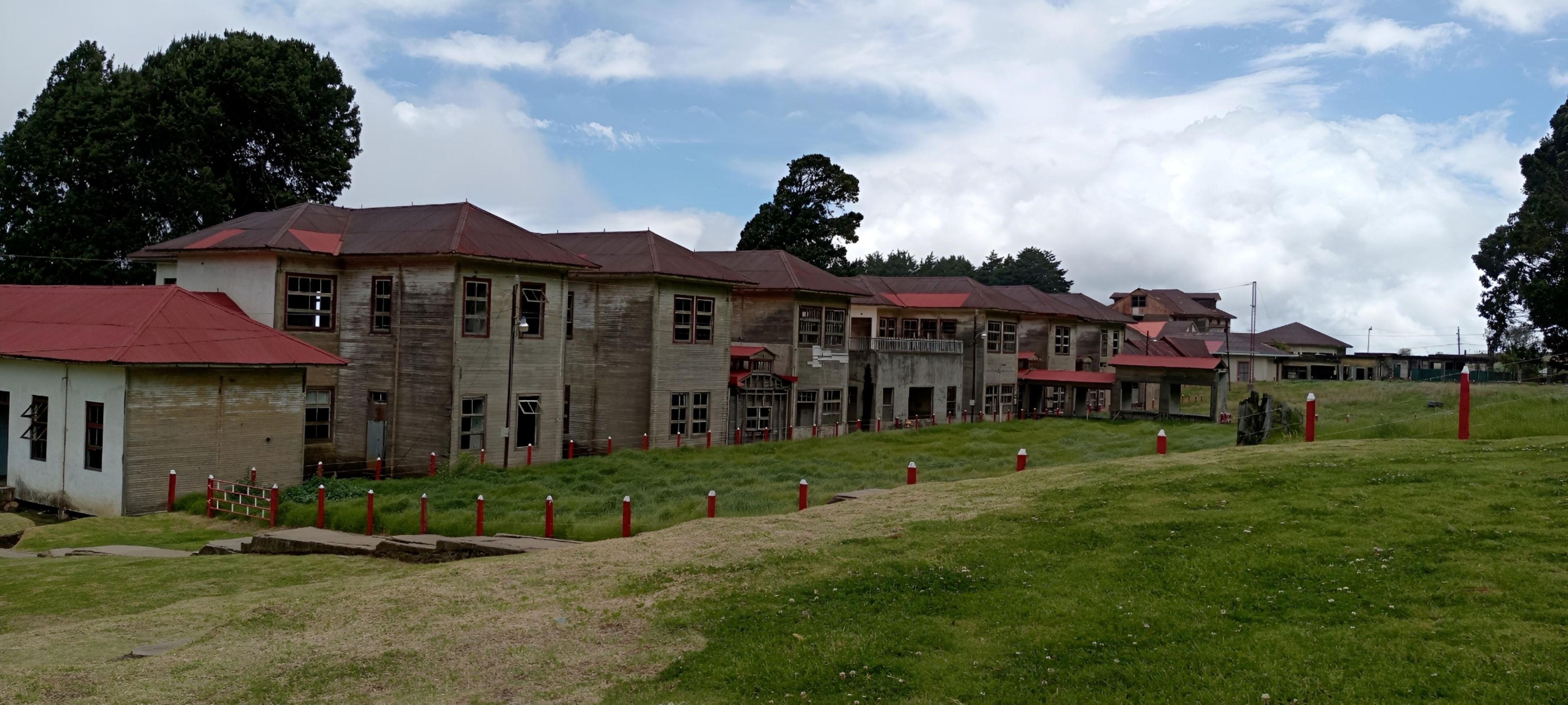 Row of abandoned wooden pavilions with rust-red roofs at the Sanatorio Durán in Costa Rica, set against an open grassy field.