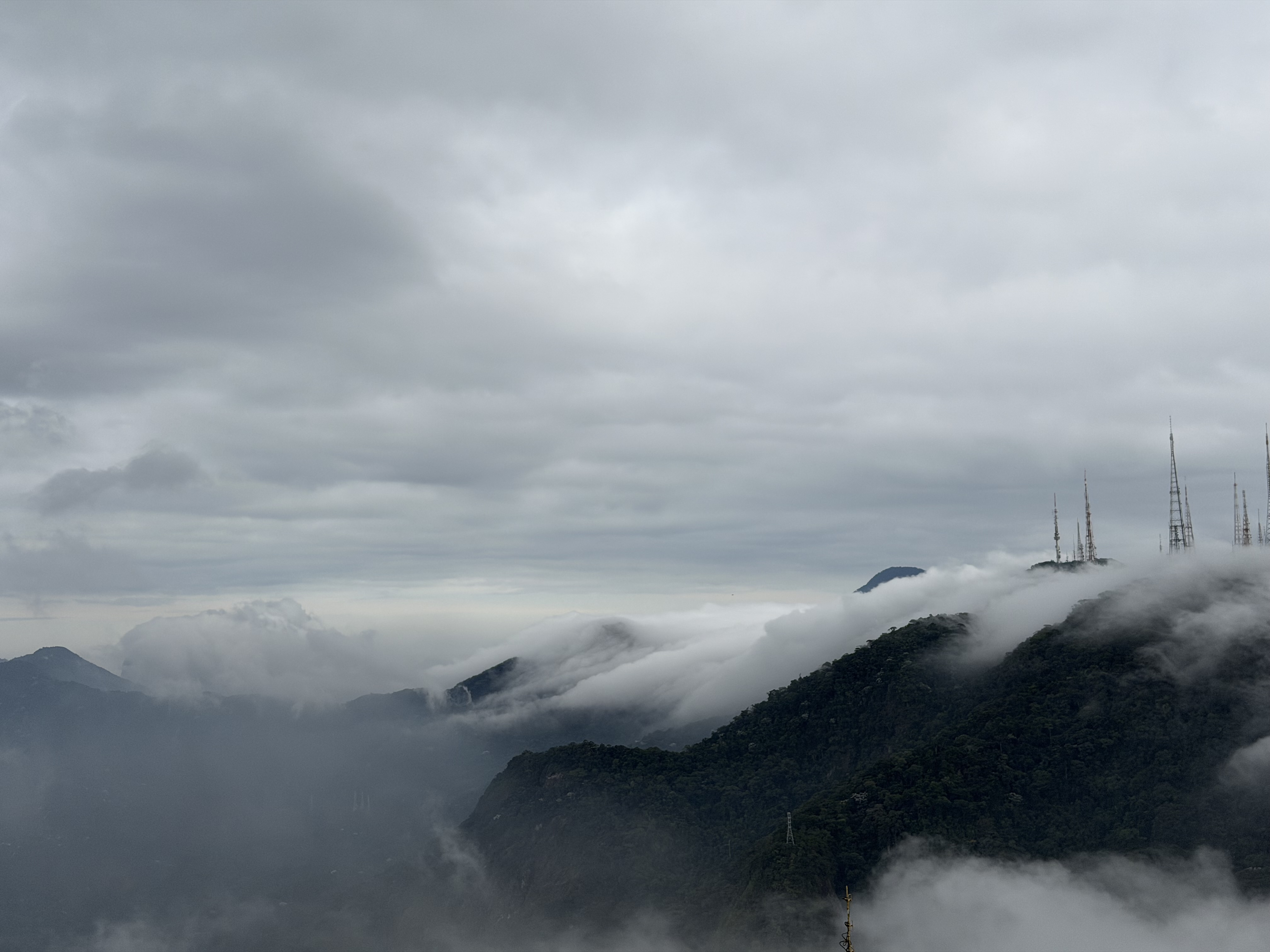 Mountain peaks covered in mist with communication towers rising above the clouds.