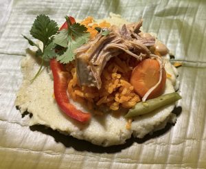 Traditional dish with orange rice and shredded meat served on a creamy base on a green leaf.