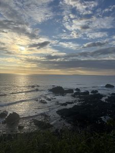 
Sunset over a rocky coastline with calm ocean waves and a colorful sky.