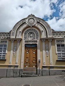 Ornate arched entrance of the Colegio Superior de Señoritas in San José, Costa Rica, featuring decorative stucco reliefs, a coat of arms medallion and a carved wooden door.
