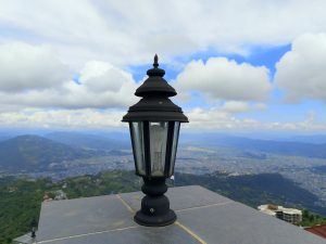 Black lantern-style lamp post on a stone ledge with panoramic view of Pokhara city and hills in the background