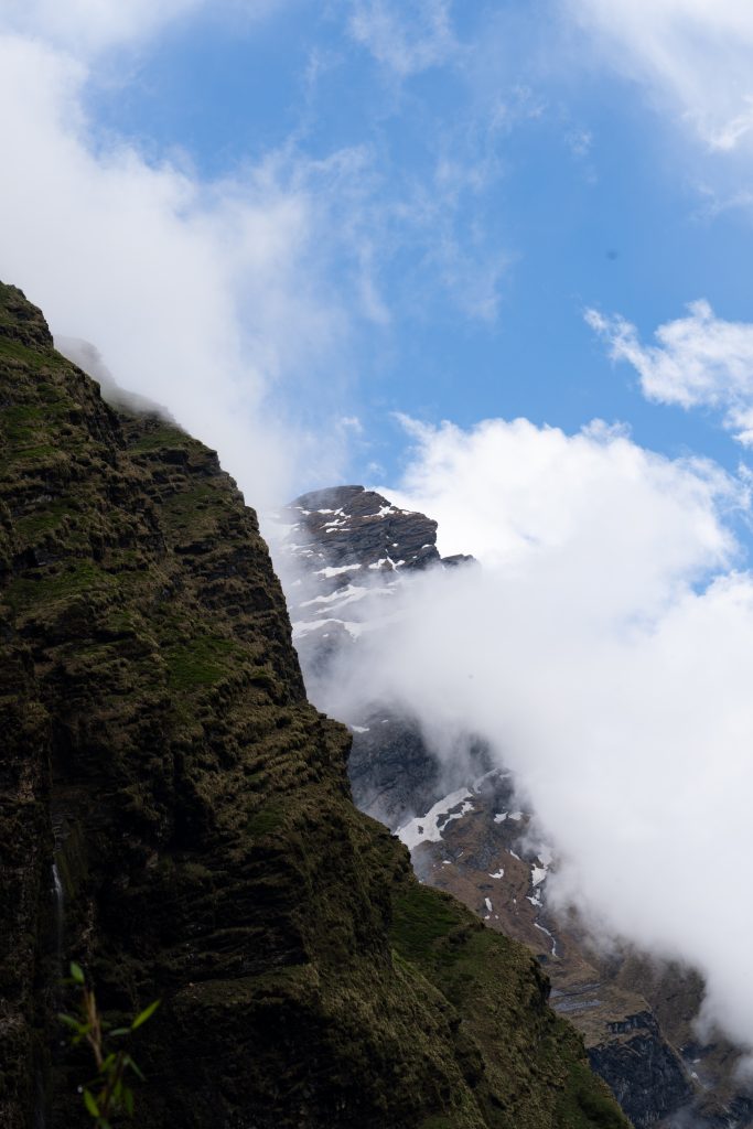 Rocky mountain slope with patches of snow, partly covered by clouds against a blue sky