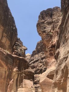 
Narrow rocky canyon with tall red and brown cliffs under a clear blue sky. 