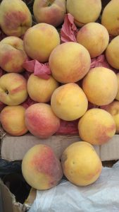 A close-up view of a pile of ripe peaches resting on pink crinkled paper within a cardboard box.
