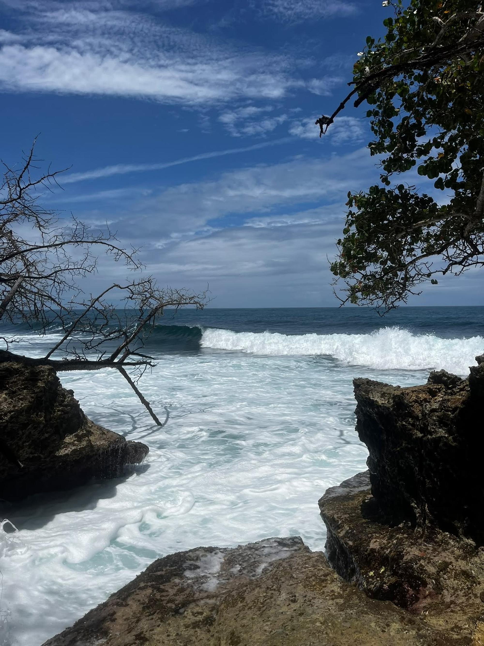 A scenic view of the ocean from a rocky shore, with frothy waves crashing against the rocks.
