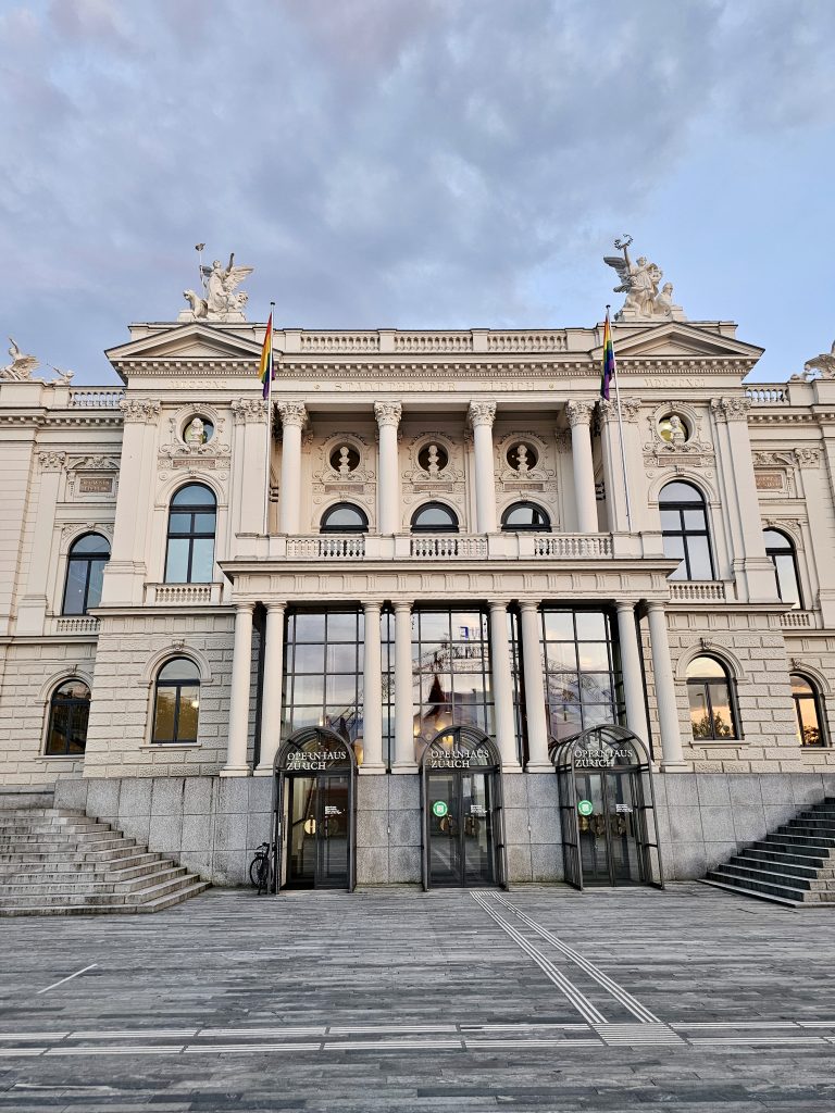 The grand façade of the Zurich Opera House, Switzerland, stands proudly with elegant columns, sculptures, and beautiful architectural details. Soft evening clouds add charm to this historic cultural landmark.