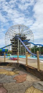 Colorful water park with large slides, a shallow pool, inflatable floats, and lounge chairs under a cloudy sky.