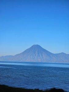 A calm lake with a large volcano rising in the background beneath a clear blue sky