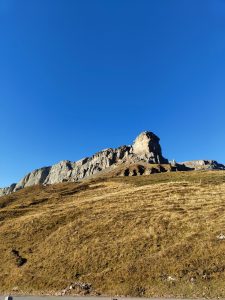 A rocky formation on a steep grassy hillside under a clear blue sky.
