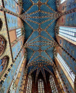 Painted Gothic vaulted ceiling with blue star patterns and stained glass windows inside St. Mary's Basilica in Kraków, Poland.