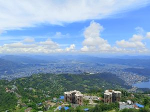 Aerial view of Pokhara city and airport runway nestled in a valley, surrounded by green hills and distant mountains under a partly cloudy sky