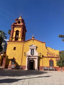 Front view of San Sebastián Mártir Church in Bernal, Querétaro, Mexico, featuring a yellow and red colonial façade under a clear blue sky.