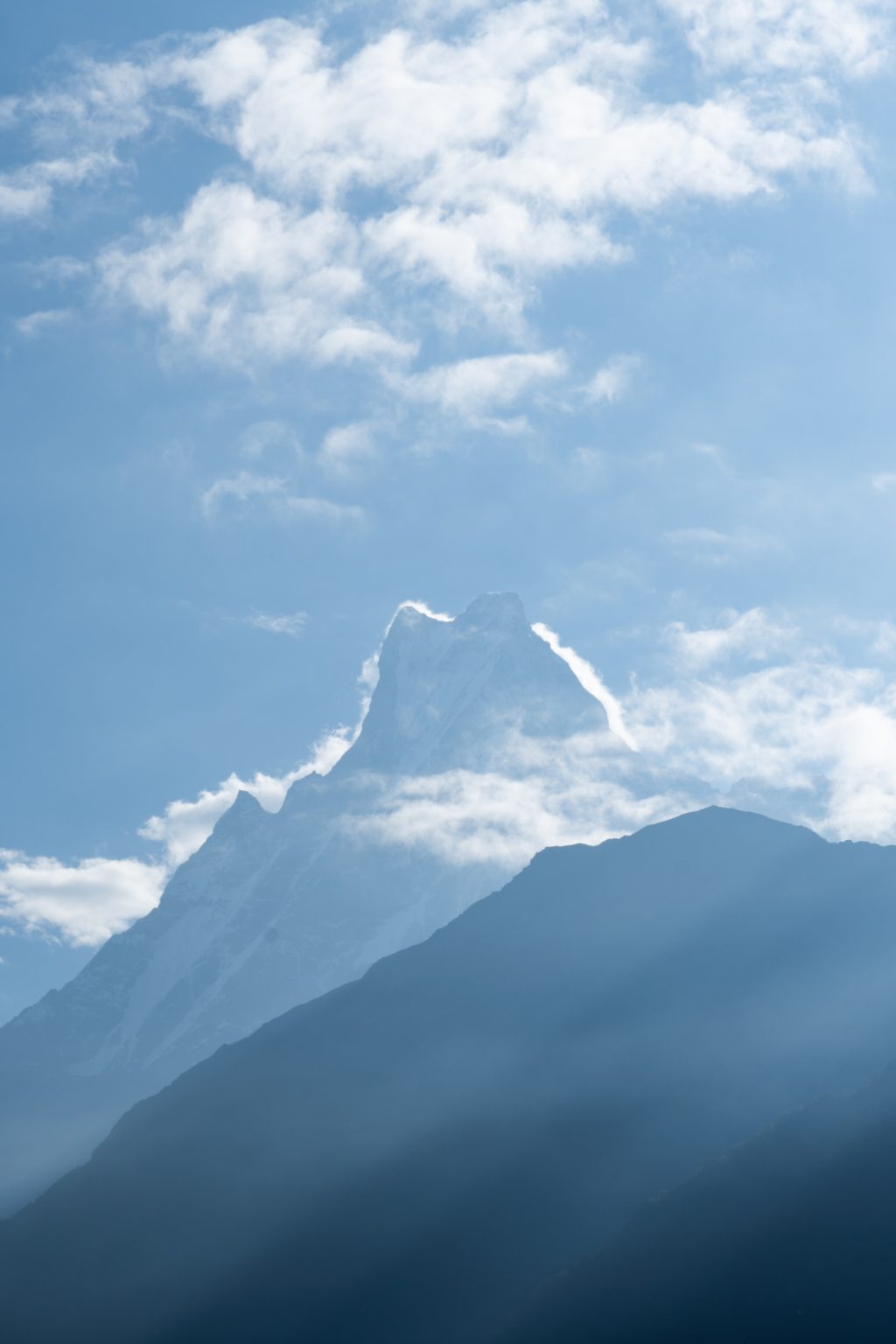 Silhouetted jagged mountain peak – Machhapuchhre’s peak, against a hazy blue sky with clouds