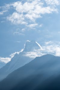 Silhouetted jagged mountain peak - Machhapuchhre's peak, against a hazy blue sky with clouds