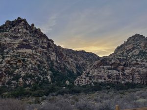 Sandstone cliffs at sunset overlooking a rugged desert landscape.
