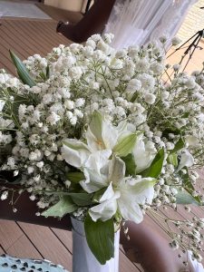 A floral arrangement featuring white lilies and baby’s breath displayed in a white vase.