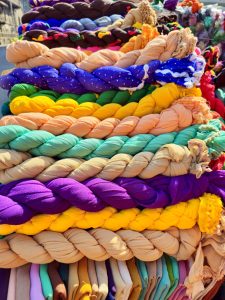 Stacks of brightly colored, rolled-up scarves (commonly known as dupattas or shawls) are neatly displayed at a roadside market, creating a beautiful mix of vibrant colors, patterns, and textures. Captured in Pune, Maharashtra.
