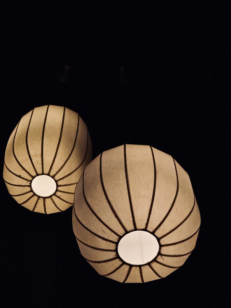 Two elegant hanging lanterns glow warmly against a dark background, creating a calm and cozy atmosphere. Their simple shape and soft light add a touch of modern interior design. Captured in Mankavu, Kozhikode.