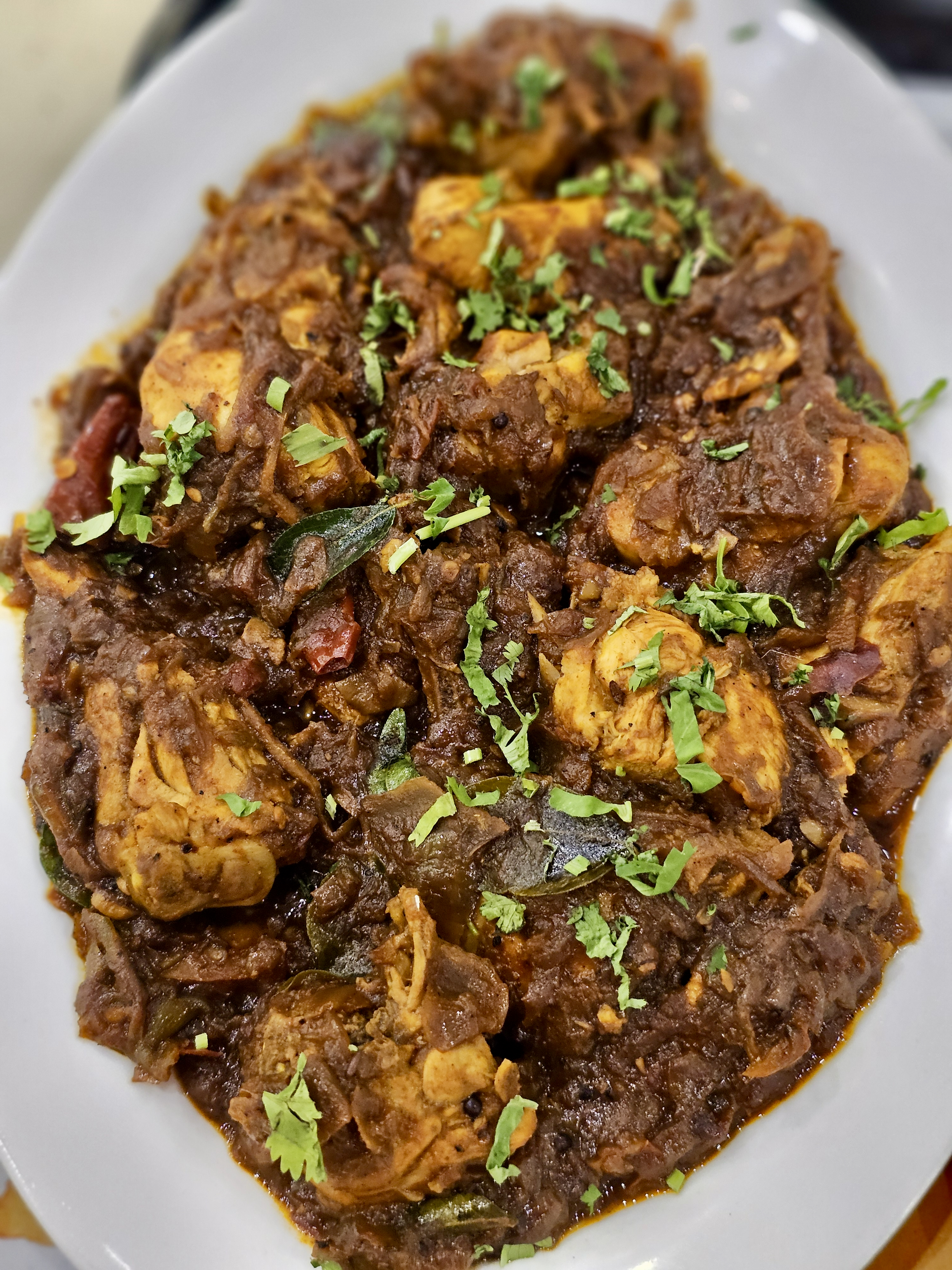 A spicy Kerala-style chicken roast cooked with onions, curry leaves, and aromatic spices. The thick masala and fresh coriander make it look flavorful and inviting. Captured in Palazhi, Kozhikode, Kerala.