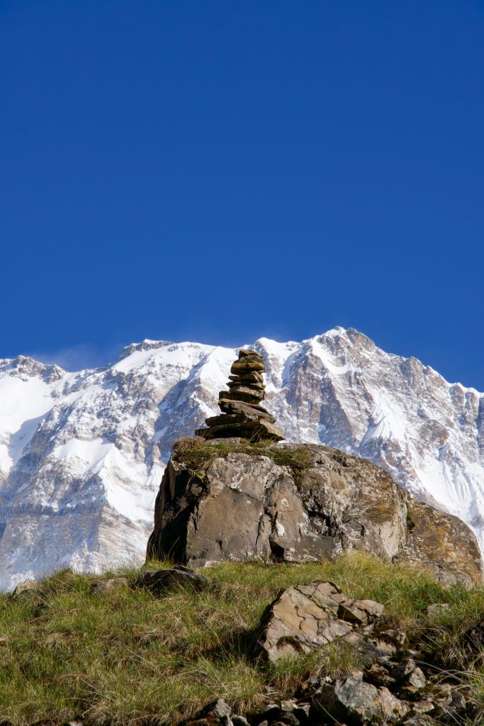 Stacked rock cairn on a boulder with grass, set against a snow-covered mountain range