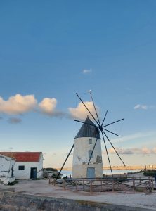 Historic windmill beside the salt flats of San Pedro del Pinatar in Murcia, Spain, beneath a blue sky with scattered clouds.
