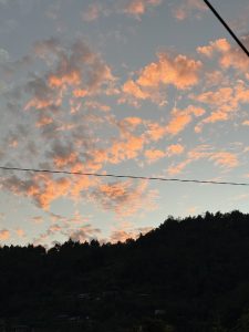 Pink and orange sunset clouds above a tree-covered hillside, with a diagonal power line crossing the tranquil evening sky.