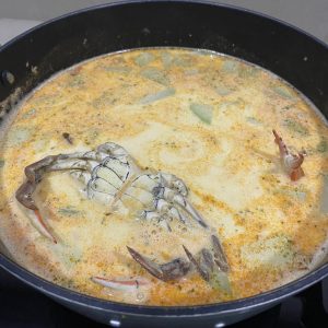 A black pot of creamy orange soup with vegetables and a large crab.