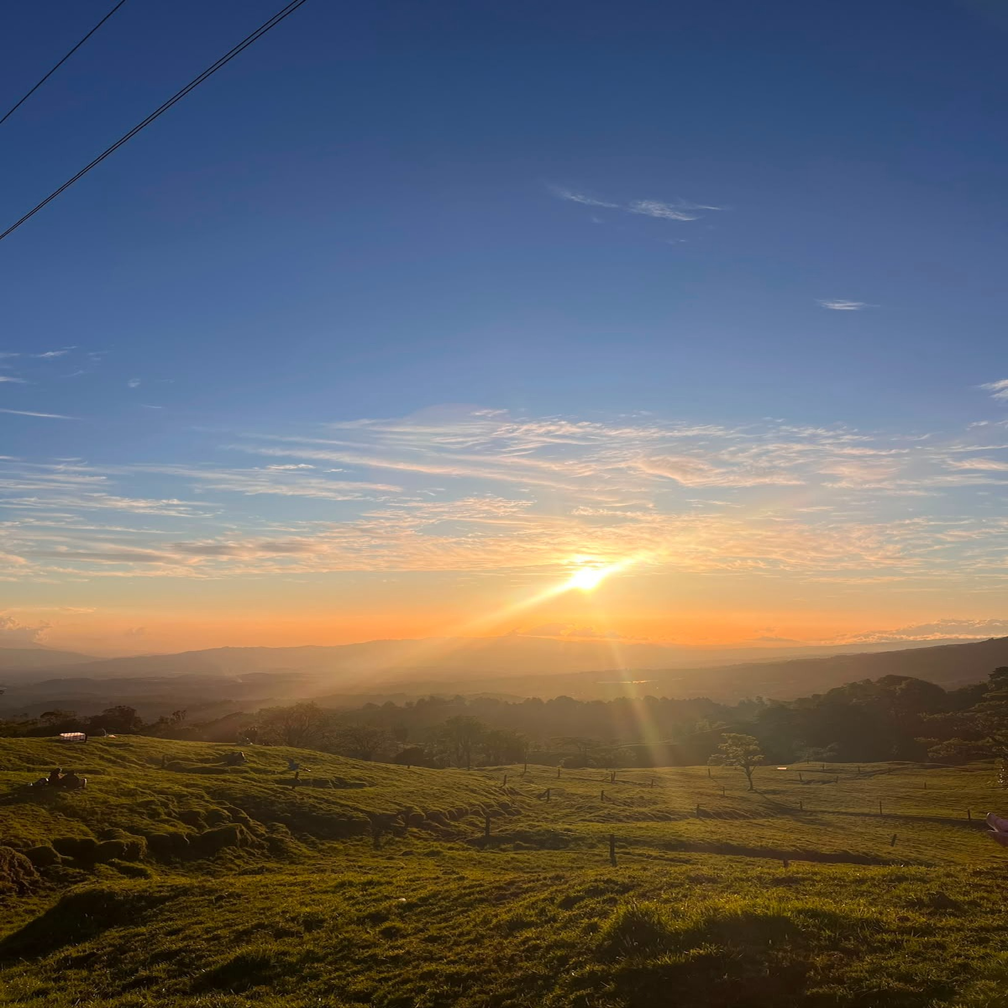 A breathtaking view of a sunset over rolling hills, with a vibrant orange and yellow light illuminating the sky.